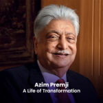 A photograph of Azim Premji, an Indian businessman and philanthropist, smiling. He has short gray hair and is wearing a suit and tie.